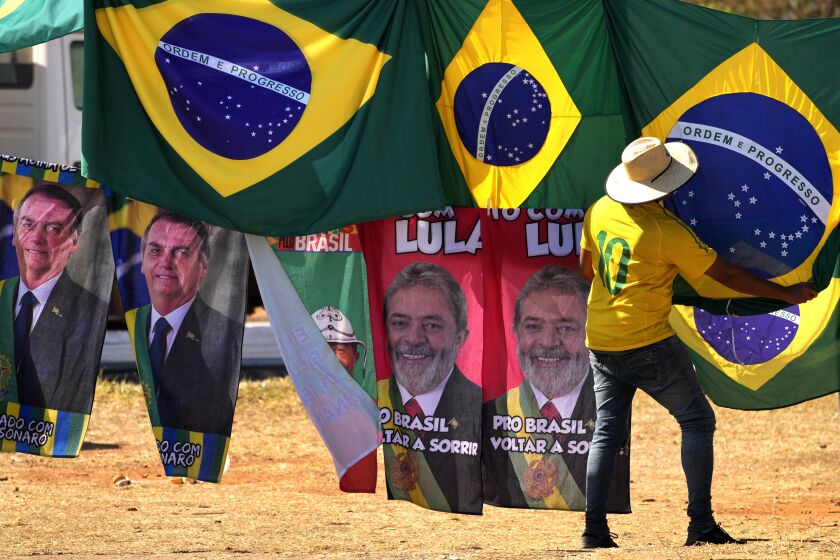 ARCHIVO - Retratos del presidente Jair Bolsonaro, a la izquierda, y del exmandatario Luiz Inácio Lula da Silva, al centro, cuelgan en el exterior de al Corte Suprema Electoral en Brasilia, abajo de banderas brasileñas, el 5 de septiembre de 2022. Bolsonaro y Lula da Silva se disputan la presidencia de Brasil. (AP Foto/Eraldo Peres, Archivo)