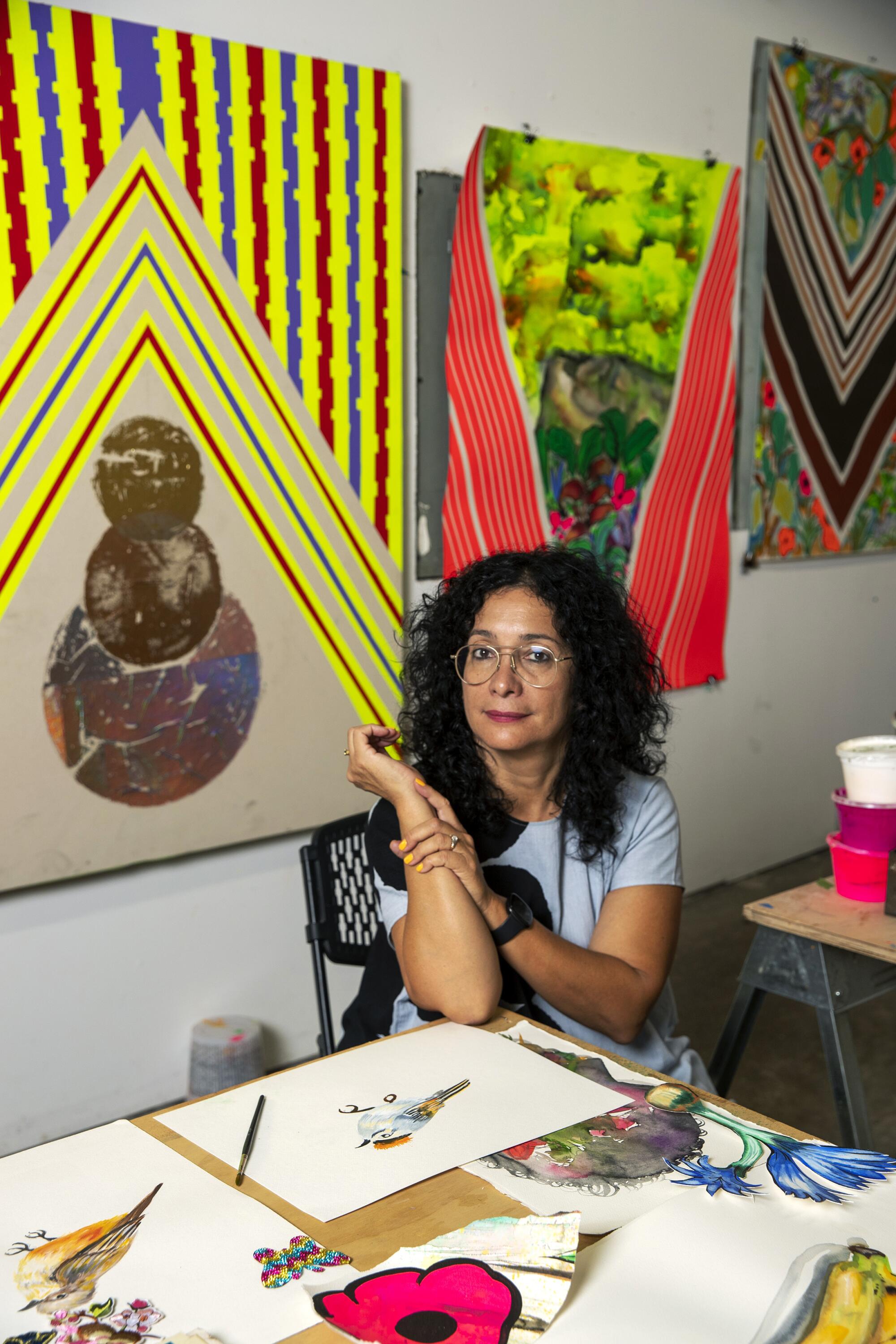 Carolyn Casta?o is seen seated in her studio, surrounded by paintings bearing bright patterns and landscape elements