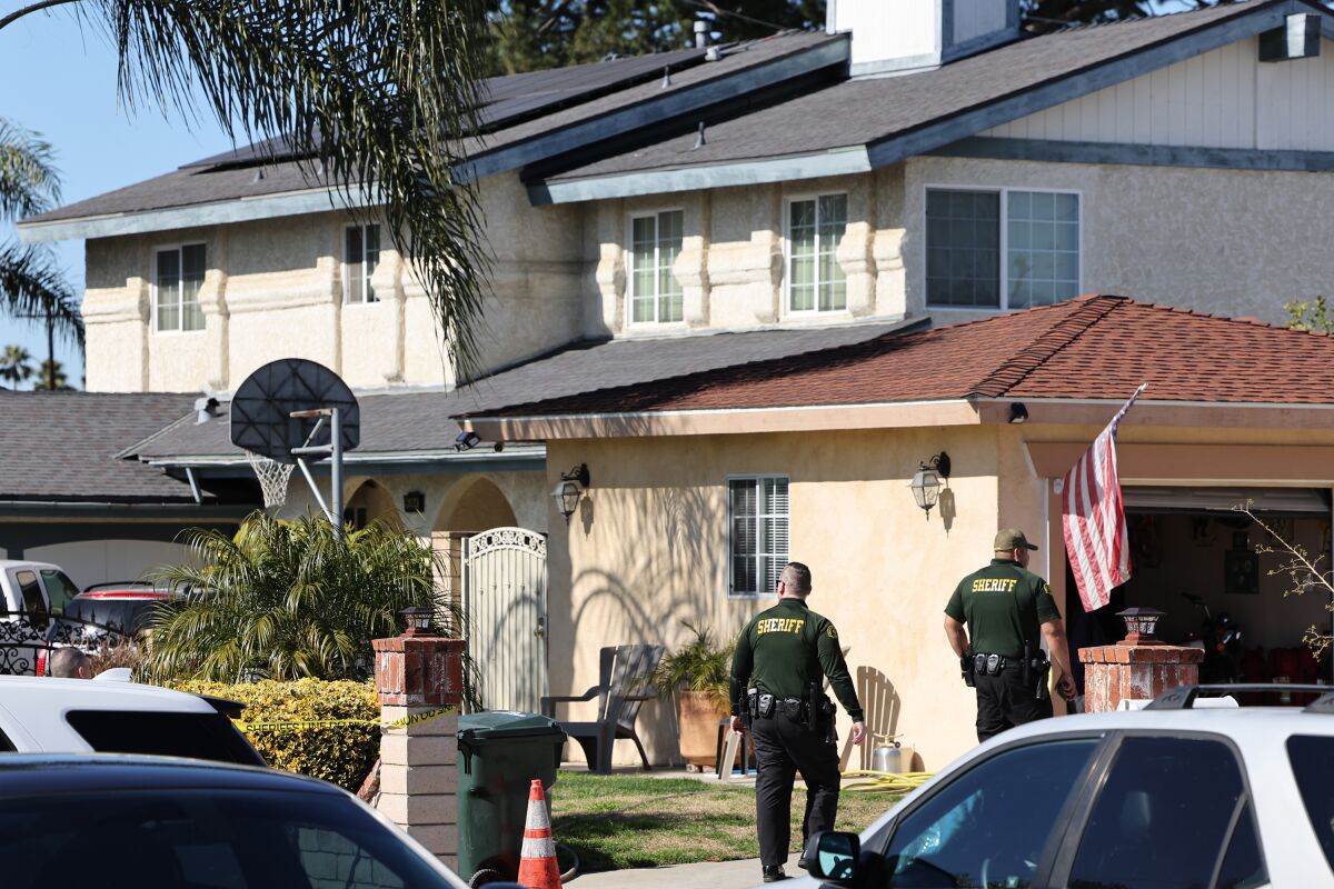 Sheriff's deputies walk up the driveway of a home with an open garage door.
