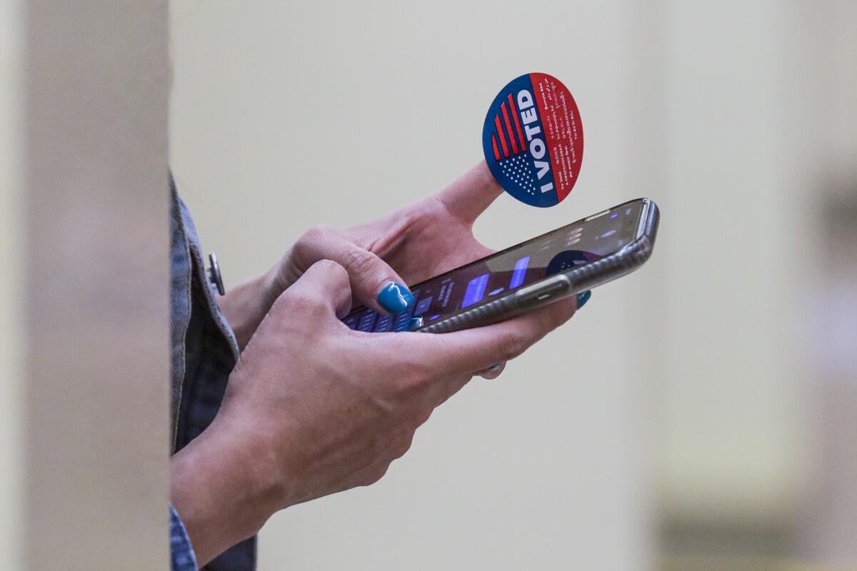An "I Voted" sticker is stuck on one finger of hands holding a smartphone