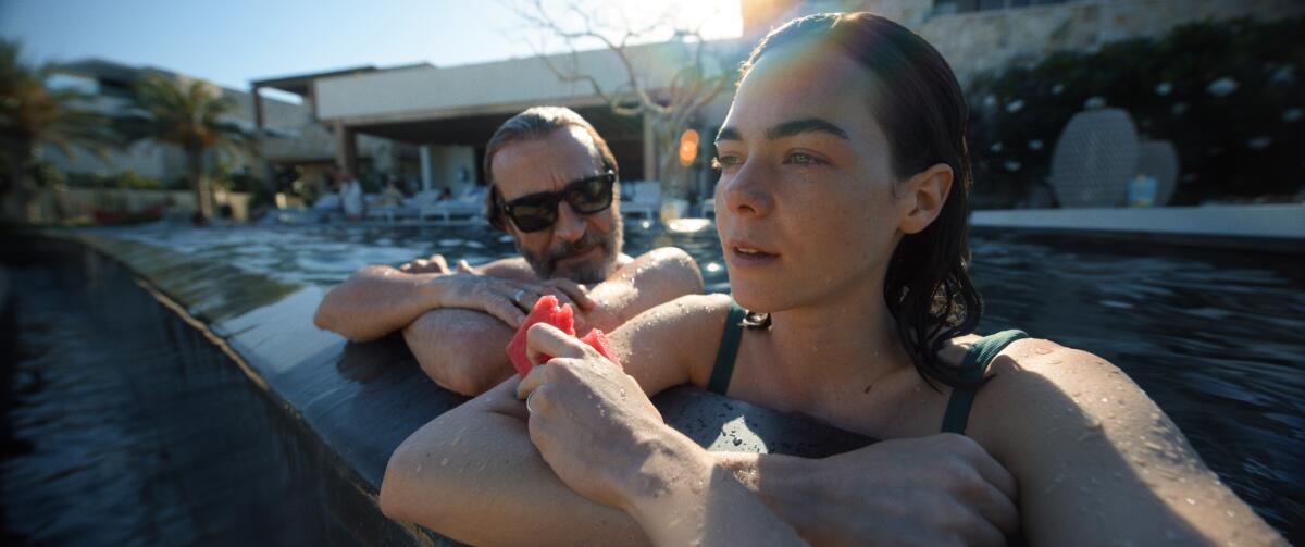 A man and woman in a swimming pool, resting with arms on its cement lip.