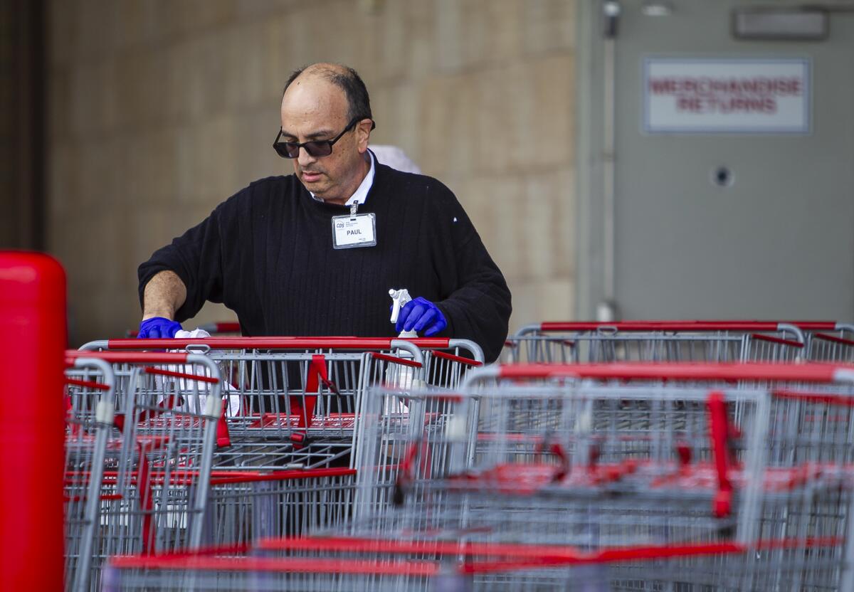 An employee at Costco in Huntington Beach disinfects shopping carts on Monday as the coronavirus outbreak began to hit some area businesses hard.