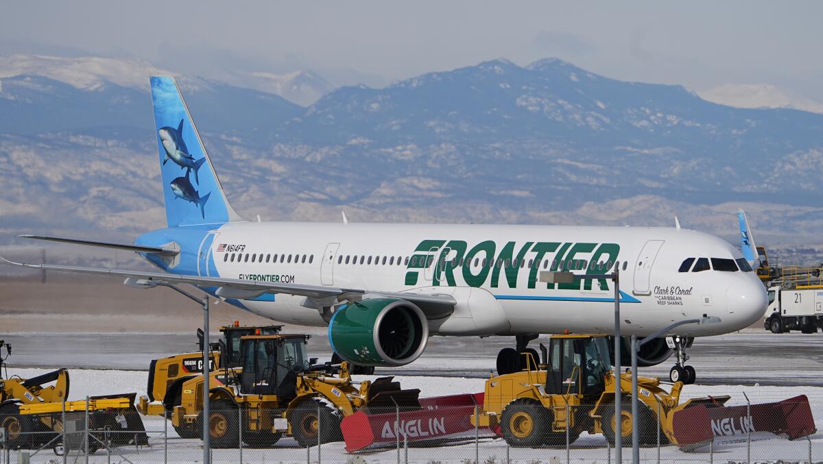 A Frontier Airlines jetliner, with mountains in the background.