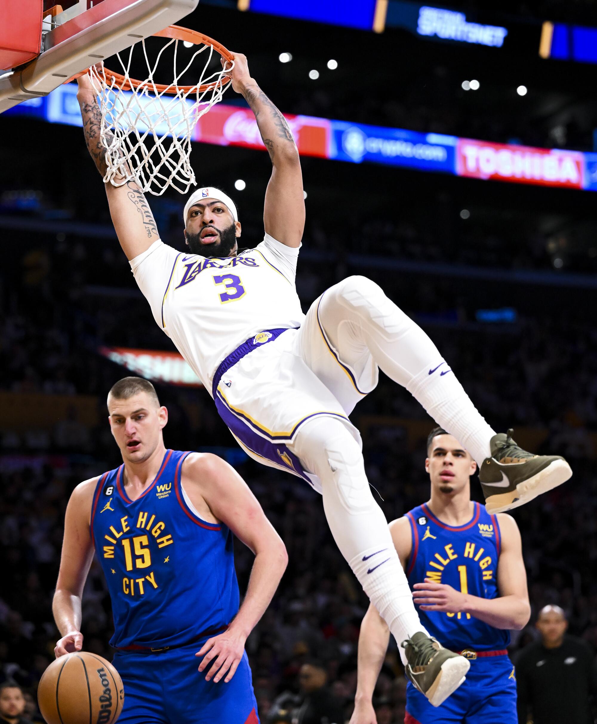 Lakers forward Anthony Davis hangs onto the rim after he dunks the ball in front of Nuggets center Nikola Jokic.