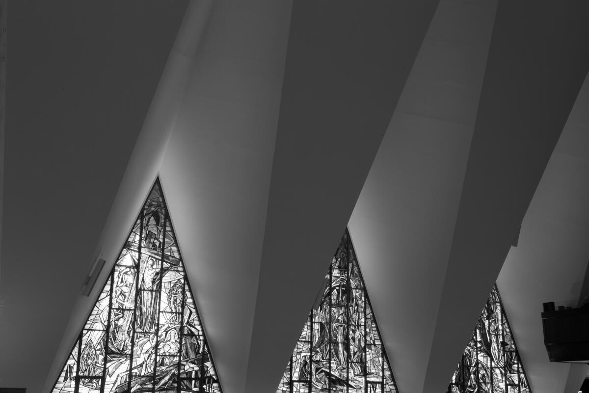 A black and white image shows a series of triangular stained glass windows amid the geometric folds of a ceiling