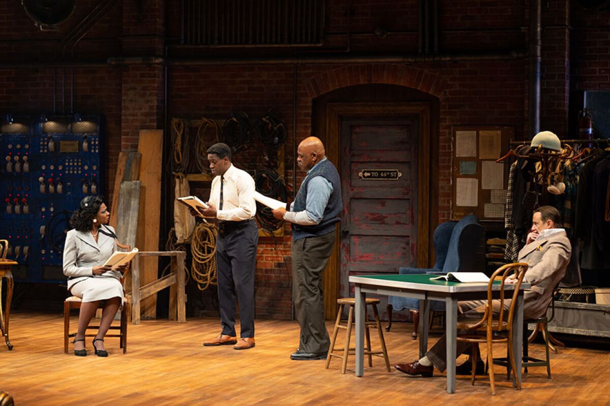 A woman and three men rehearse a scene onstage with their scripts.