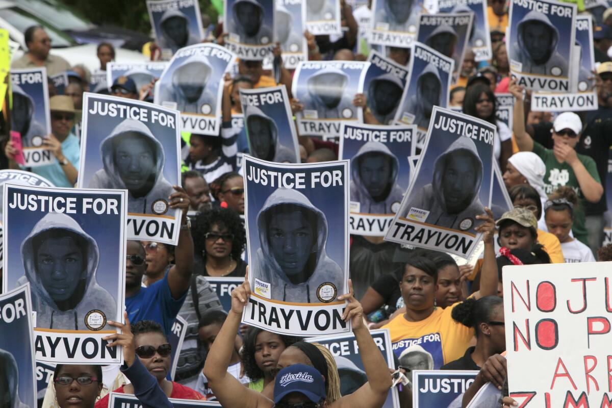 Protesters hold signs with a photo of a young boy wearing a hoodie and the words "justice for trayvon"