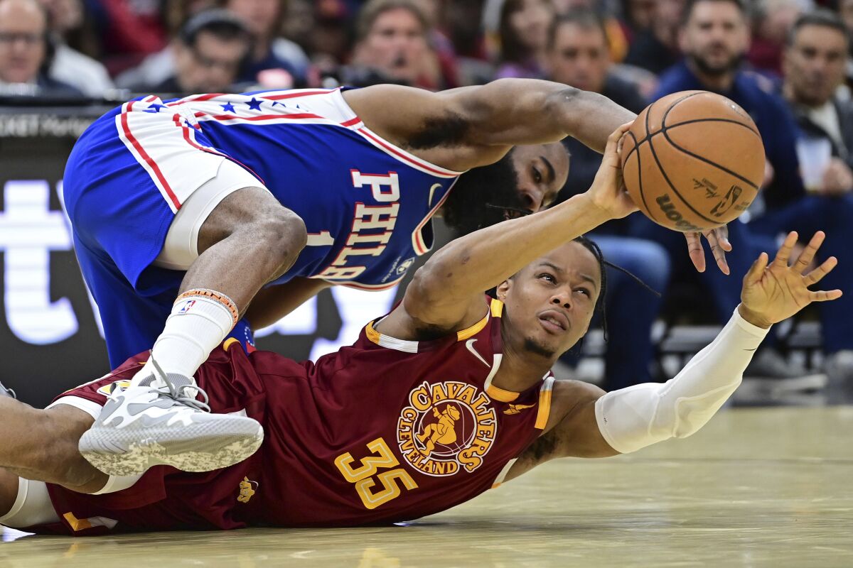 Cleveland Cavaliers forward Isaac Okoro (35) passes the ball while he scrambles on the floor with Philadelphia 76ers guard James Harden, top, in the second half of an NBA basketball game, Sunday, April 3, 2022, in Cleveland. AP Photo/David Dermer)