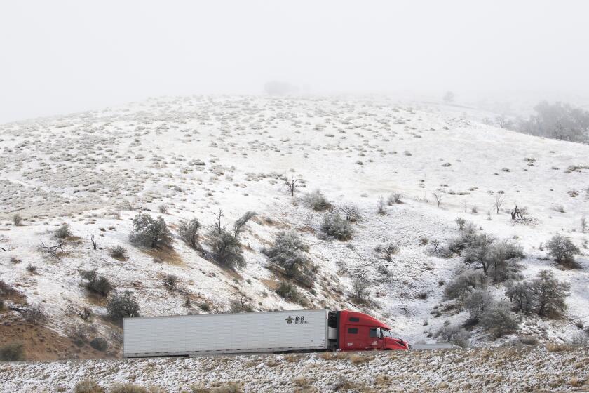 LEBEC, CA - DECEMBER 14: Traffic flows on Interstate 5 past snow-covered hills in Lebec, CA on Tuesday, Dec. 14, 2021. A cold storm moved through bringing rain and snow to Southern California. (Myung J. Chun / Los Angeles Times)