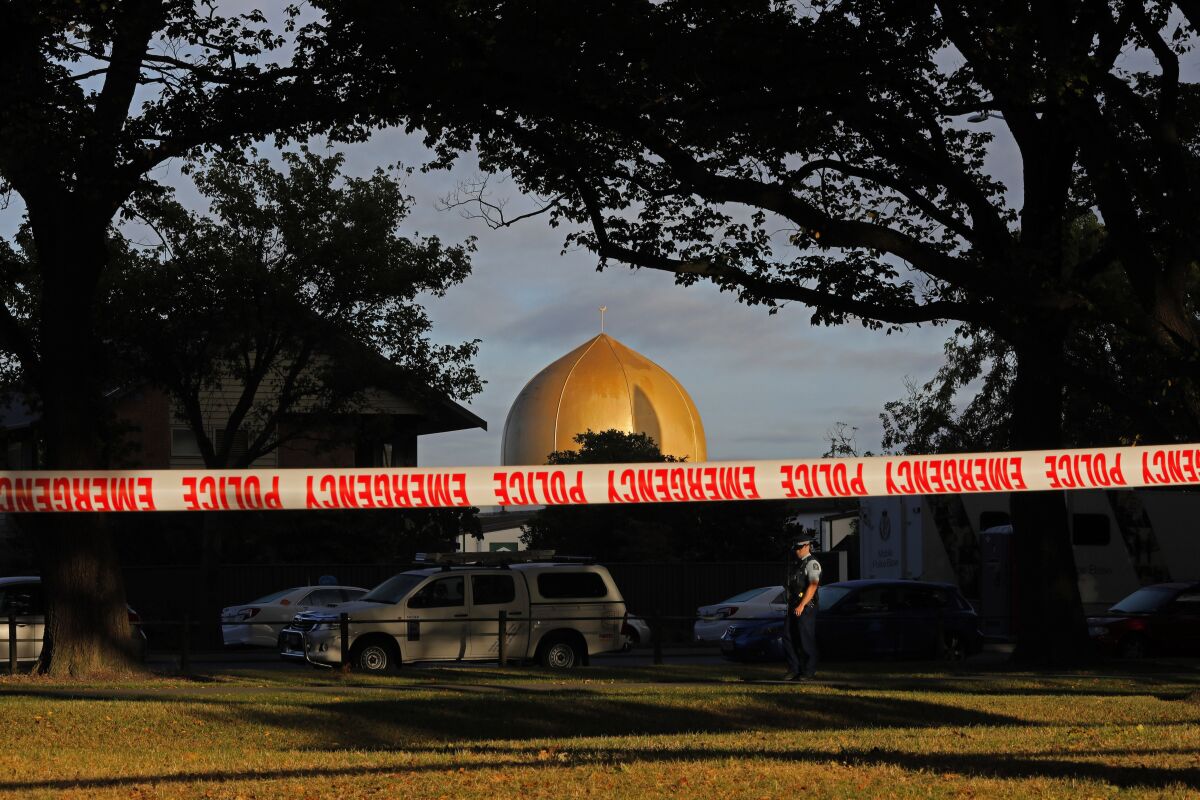 Police tape blocks off an area where an officer stands guard, the dome of a mosque in the background.
