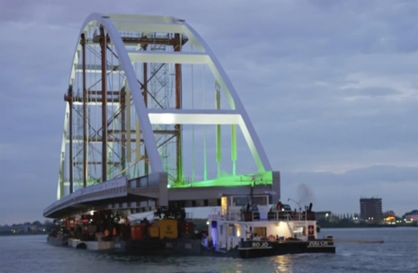 In this image taken from video released by Netherlands Department of Waterways and Public Works, showing a 200-metre (656-feet) long bridge taking a slow cruise through the heart of Rotterdam as it heads towards its new temporary home near the city's busy port area early Monday May 10, 2021 in Rotterdam. Tug boats moved the 20 metres (65 feet) wide and with a 40 metre (131 feet) high arch, Suurhoff Bridge early on Monday supported on pontoons under a series of other bridges on the Maas River that bisects the Dutch city. (RIJKSWATERSTAAT Department of Waterways and Public Works via AP)