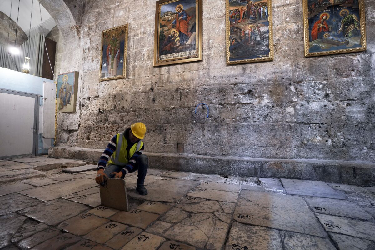 A member of the restoration team removes a stone from the floor of the Church of the Holy Sepulchre, where many Christians believe Jesus was crucified, buried and rose from the dead, in the Old City of Jerusalem, Thursday, March 17, 2022. The three Christian communities that have uneasily shared their holiest site for centuries are embarking on a project to restore the ancient stone floor of the Jerusalem basilica. The project includes an excavation that could shed light on the rich history of the Church of the Holy Sepulchre in the Old City. (AP Photo/Mahmoud Illean)