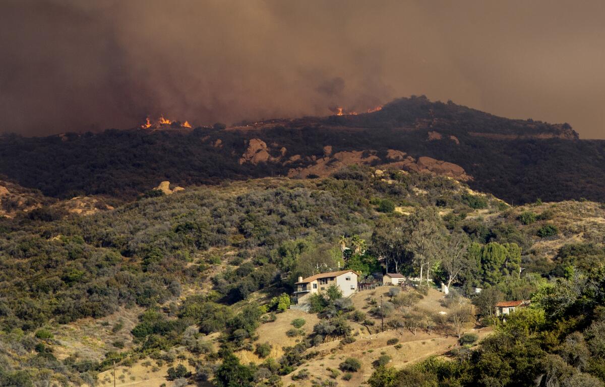 Flames shoot up from a wildfire in rugged terrain near homes 