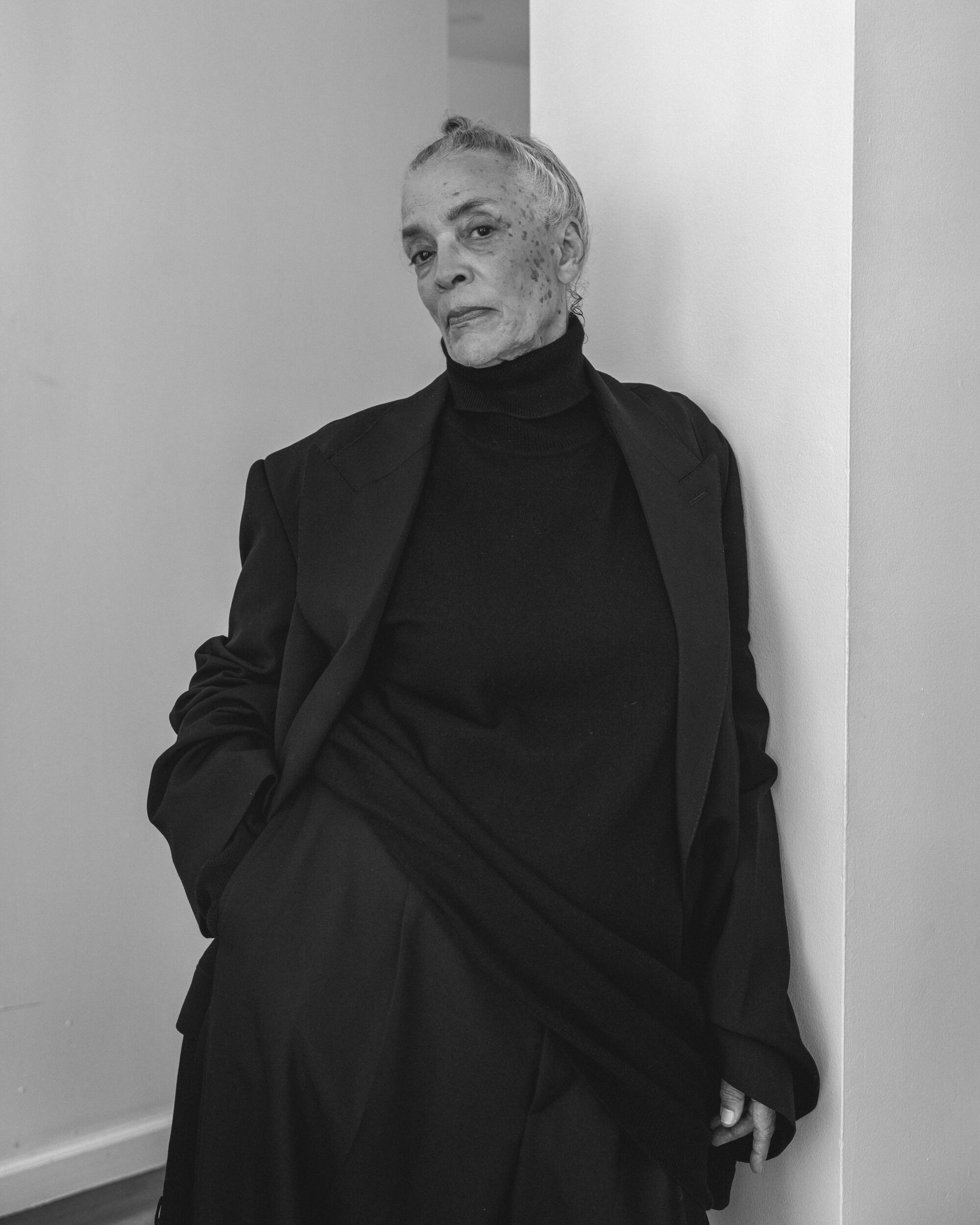 A black and white photo of a woman in a black turtle neck and black jacket.