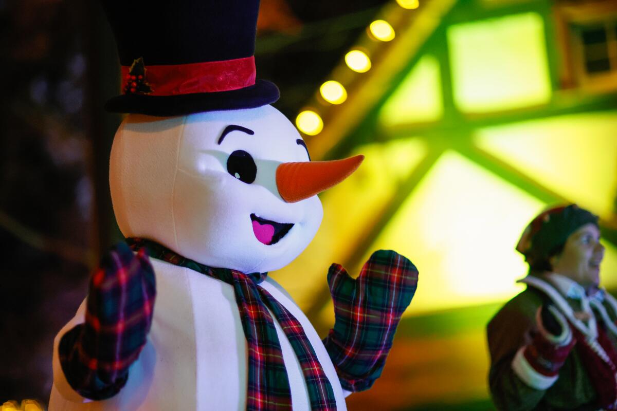 A person in a snowman costume walking around a Christmas village at night.