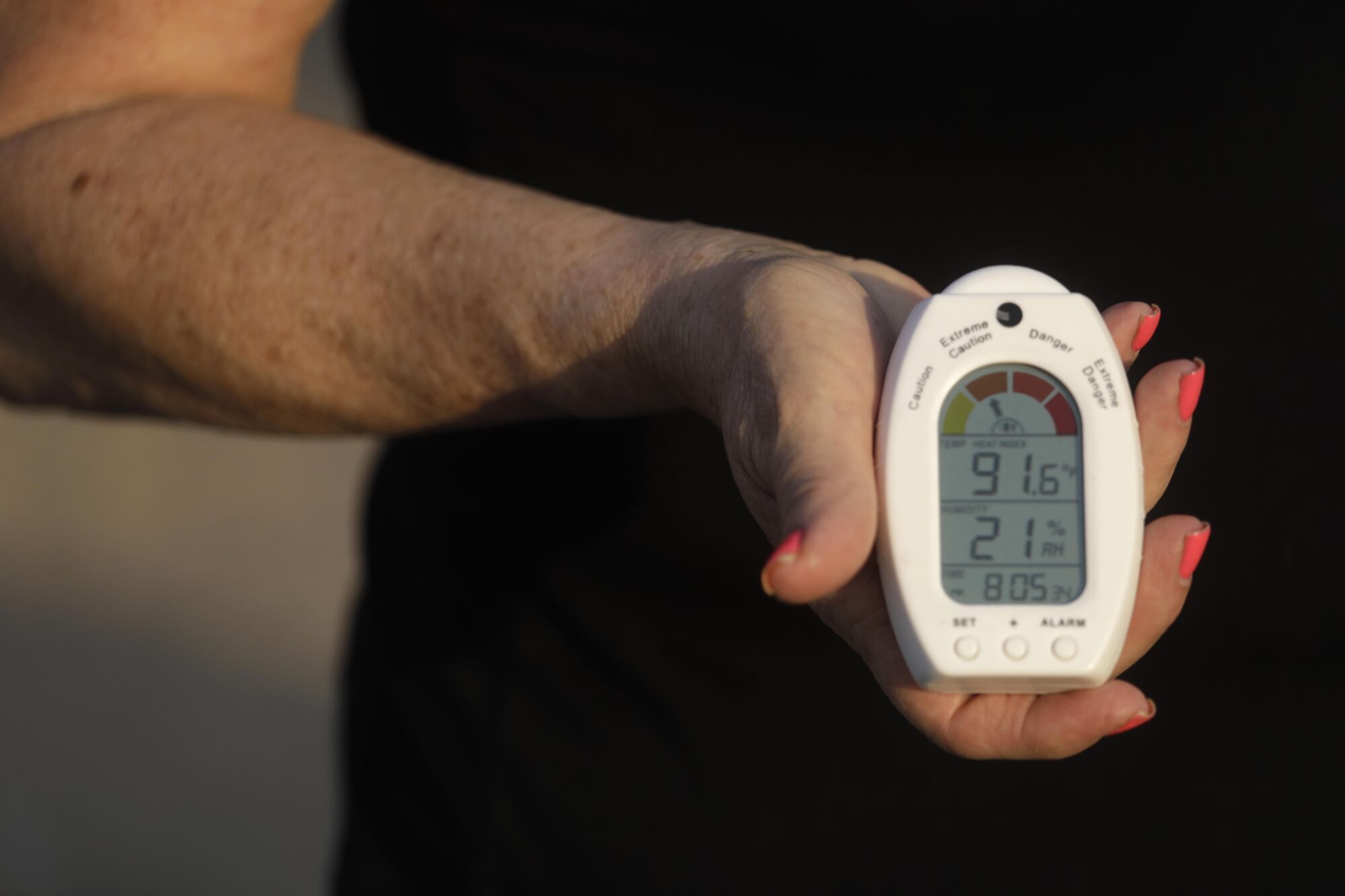 A woman's hand holds a thermometer with a display showing an outdoor reading of 91.6 degrees