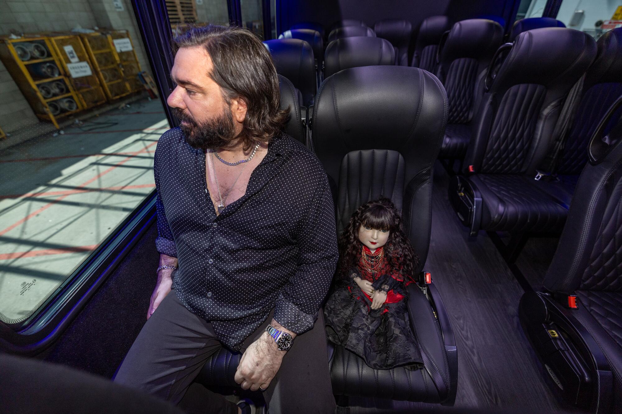 A man shares a bus seat with a small prop doll.