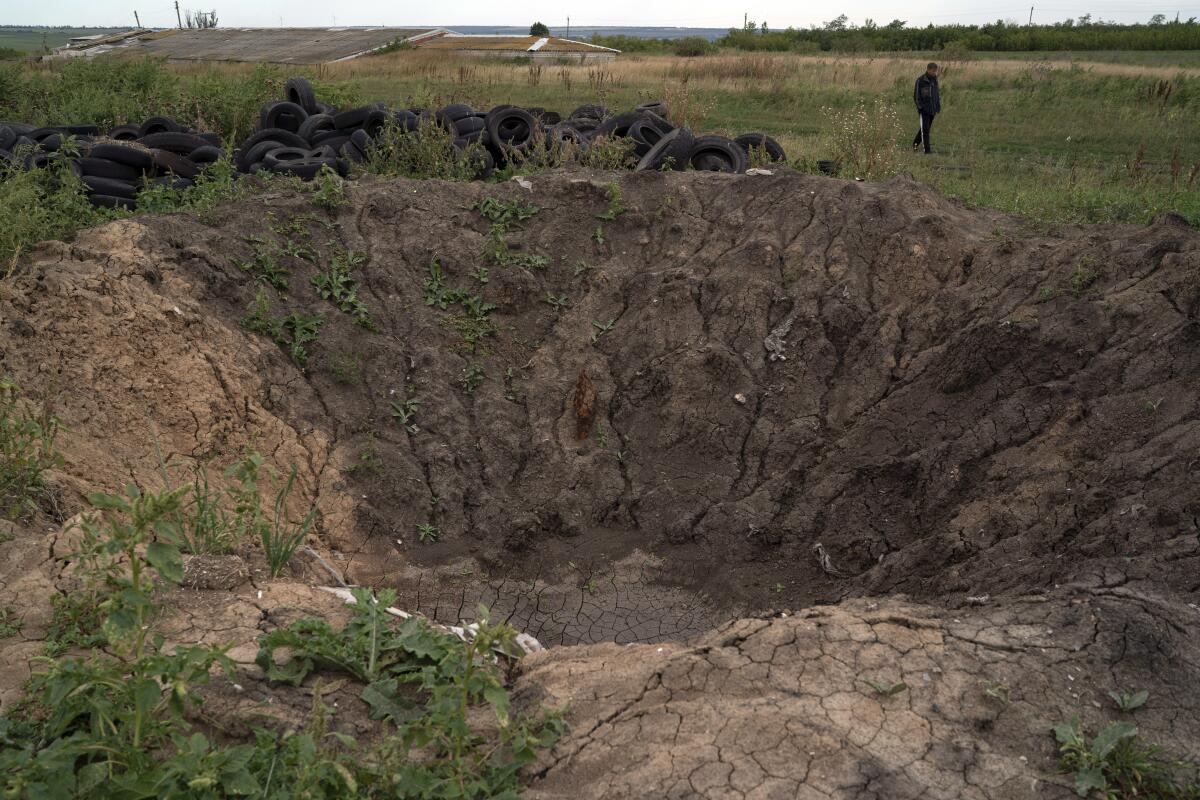 Un trabajador pasa junto al cráter dejado or una explosión en un campo en la granja Veres, 