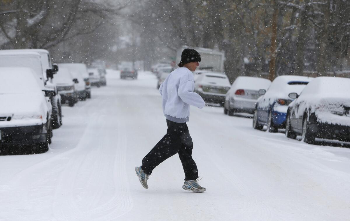 A jogger steps carefully across a snow-covered street Wednesday morning in Denver.