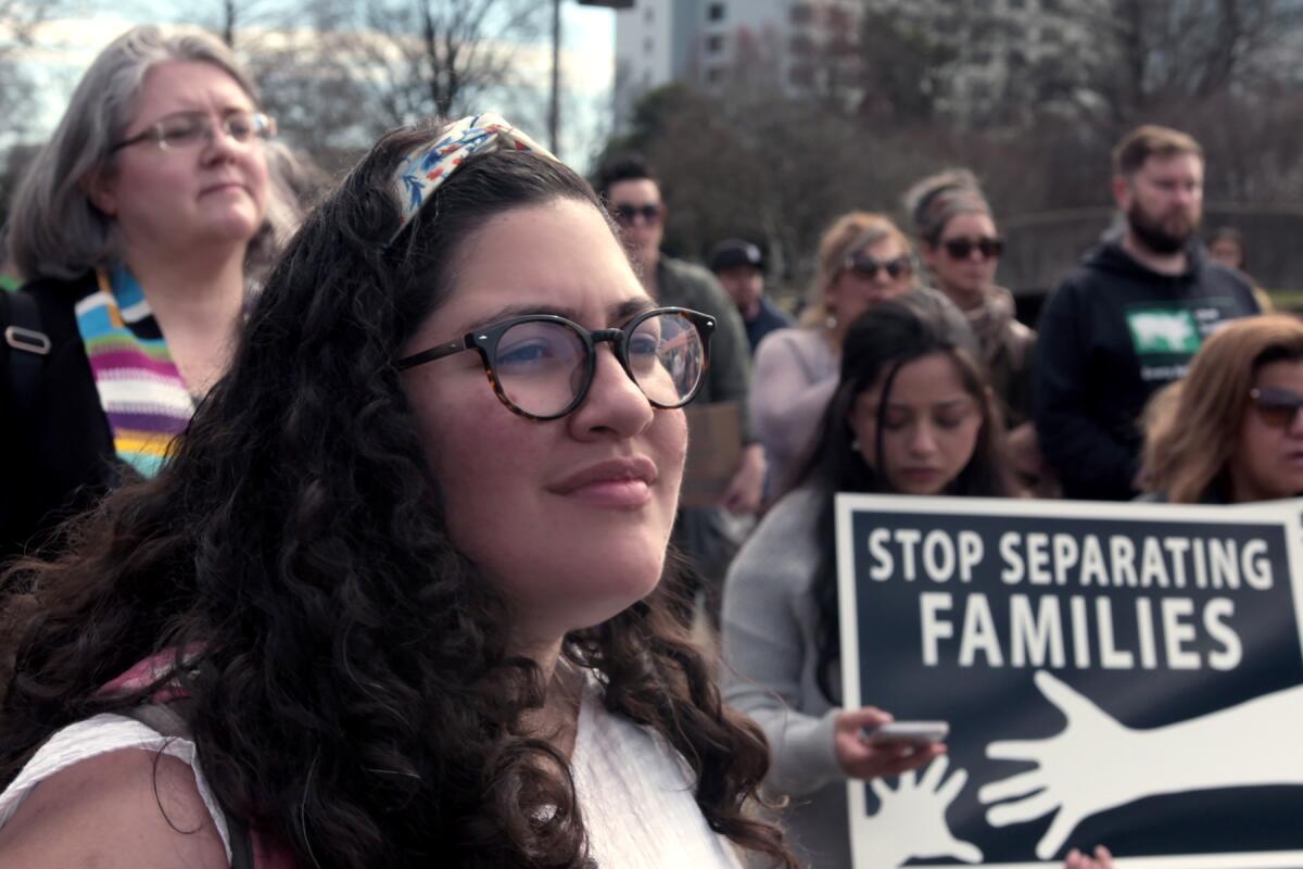 A woman at a protest stands in front of people holding a sign that reads "Stop separating families."