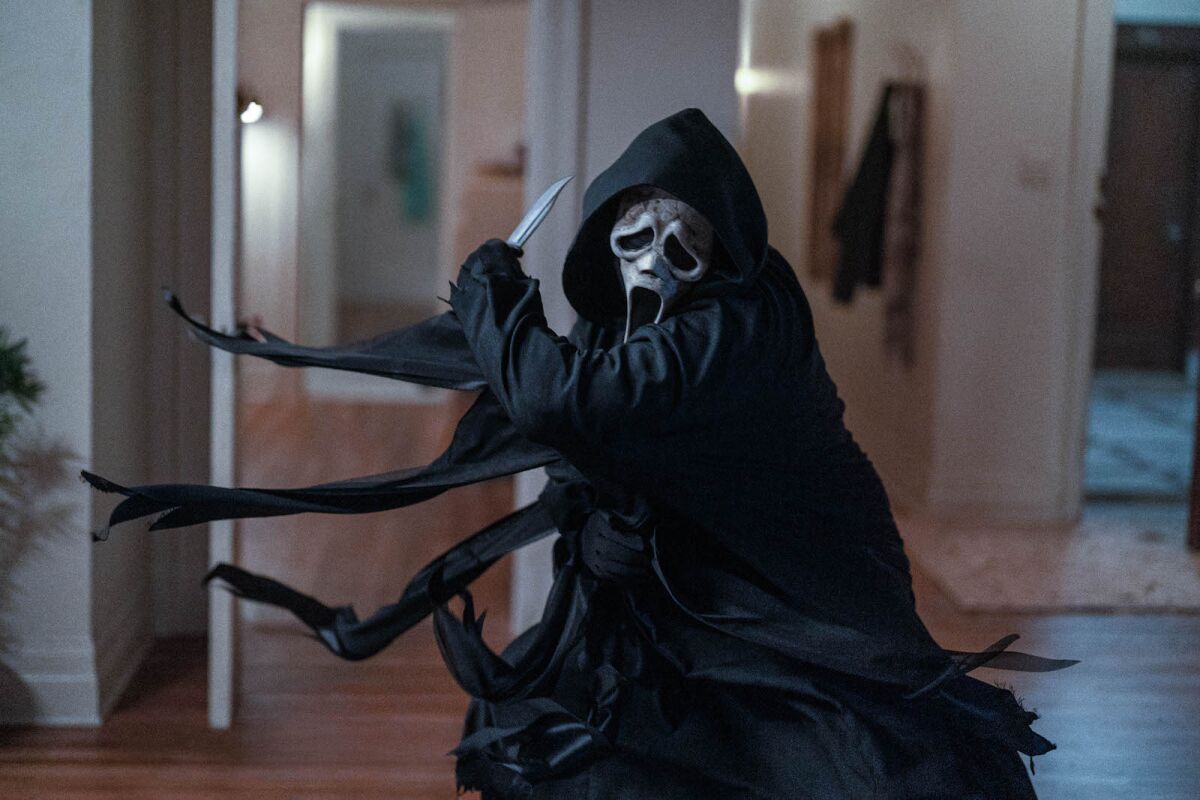 Ghostface brandishes a knife in an apartment.