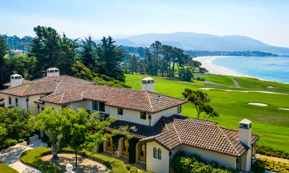 A mansion surrounded by trees that overlooks a golf course and the ocean.