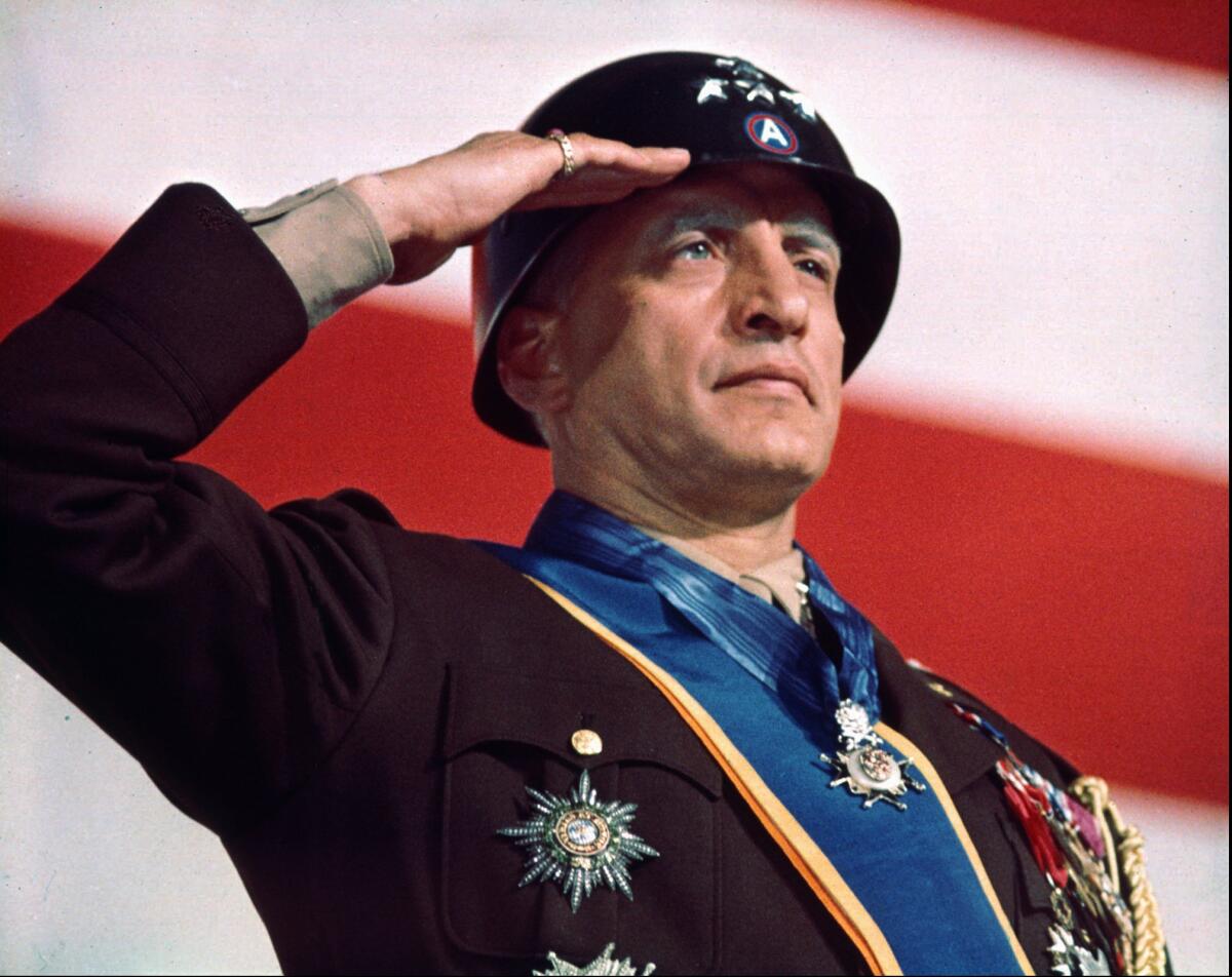 A highly decorated military man salutes with a U.S. flag behind him.