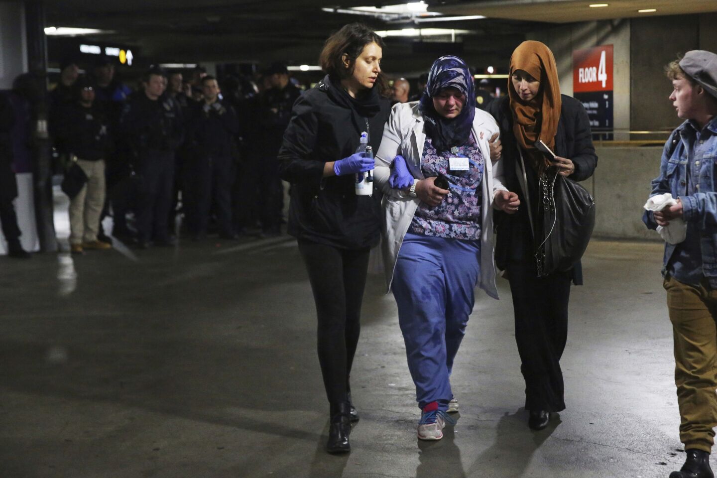 Saffiya Hrahsheh, center, is helped away from police by Liz Bates, left, and others after being pepper sprayed by officers breaking up protests early Sunday at Seattle-Tacoma International Airport.