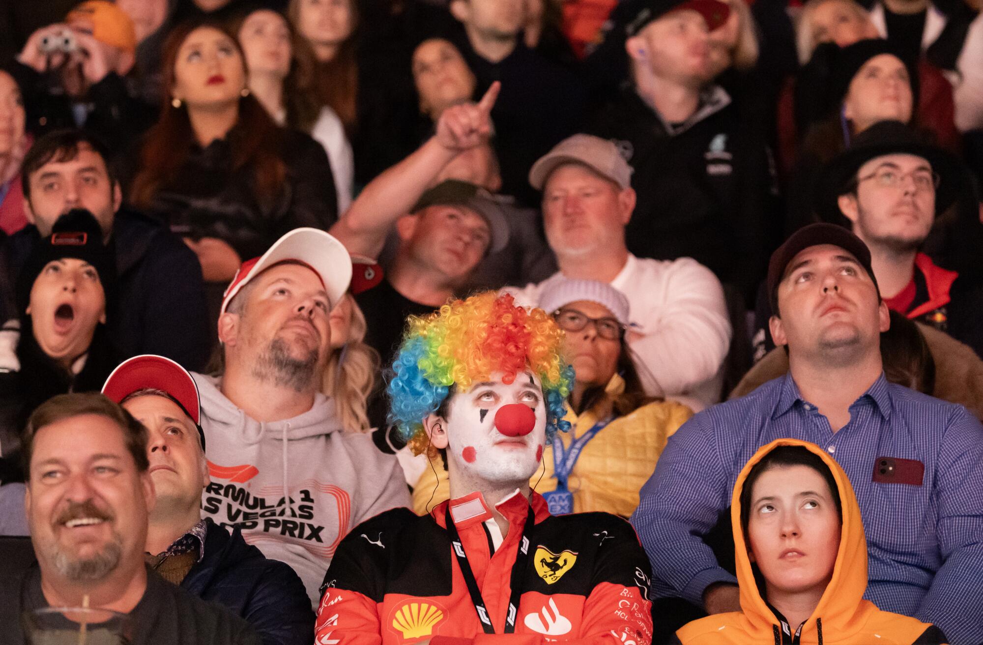 A Ferrari fan in clown makeup watches the qualifying session among spectators.