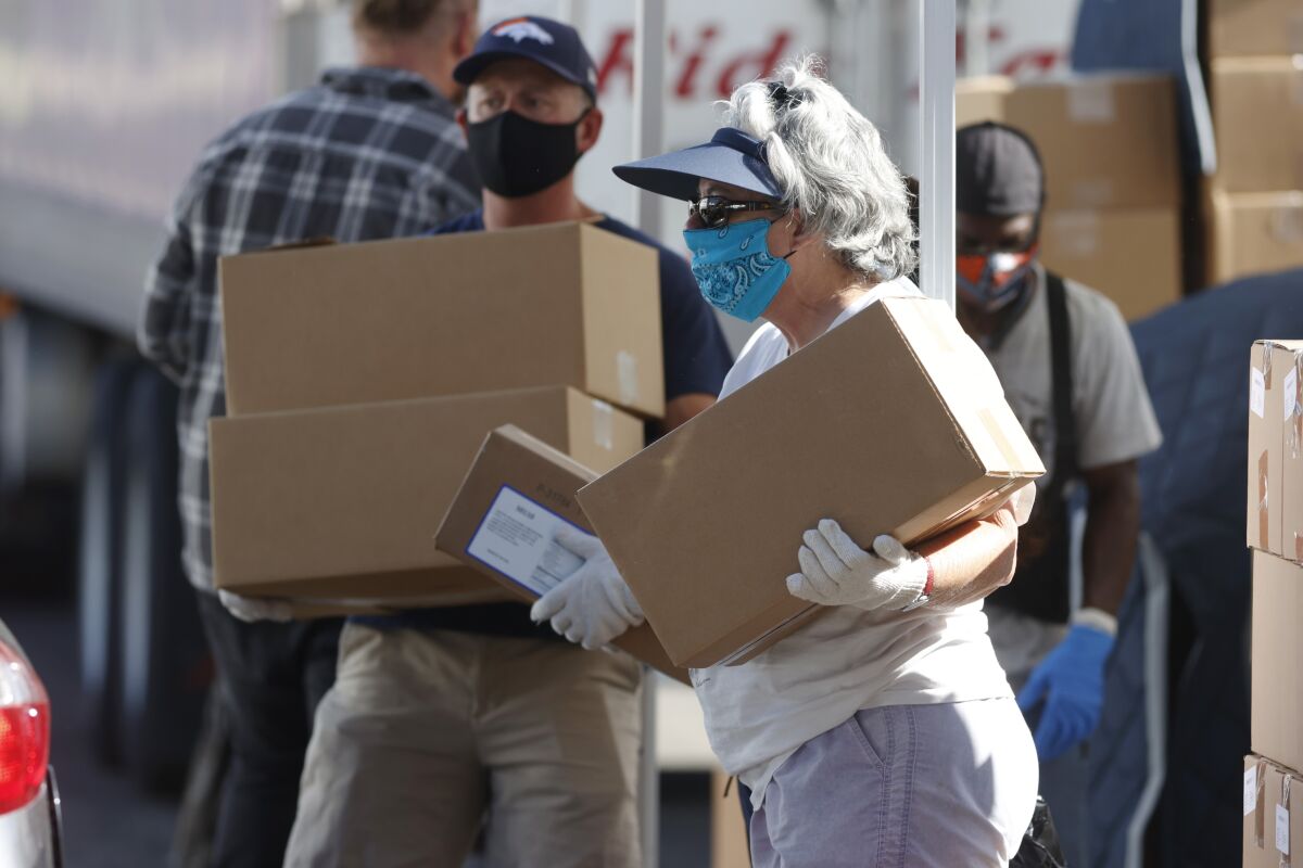 Volunteers carry boxes of food at a large mobile pantry set up by the Food Bank of the Rockies in Denver.
