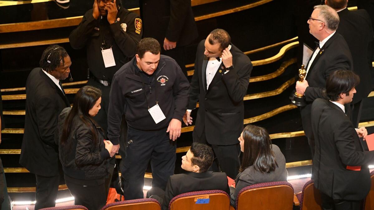 An EMT (standing, center) speaks with Rami Malek (seated, center) during the 91st Academy Awards, after the lead actor winner slipped near the stage.