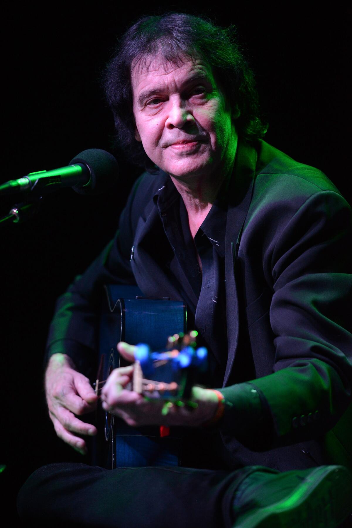 Dwight Twilley plays a guitar in front of a microphone.