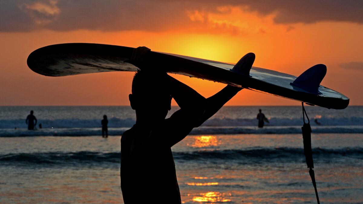 A surfer carries a board at sunset along Kuta Beach on the Indonesian resort island of Bali.