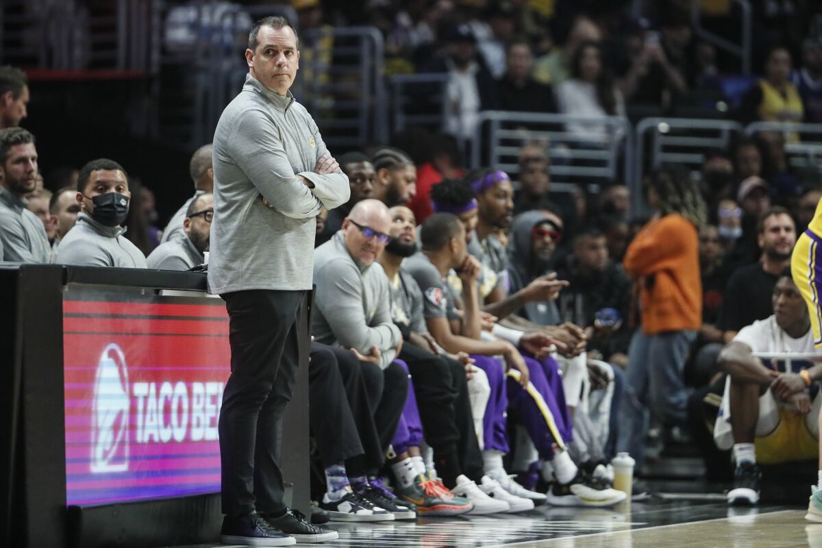 Lakers coach Frank Vogel stands in front of the team's bench with his arms folded.