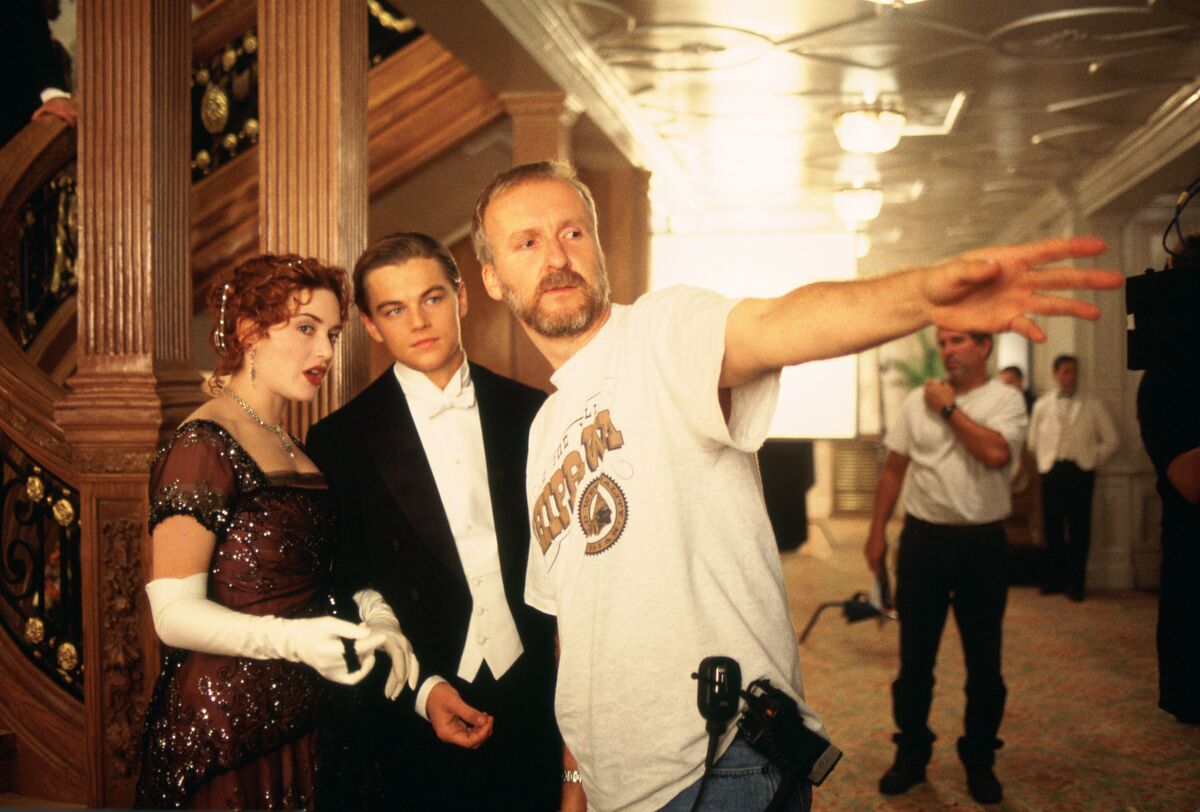 A movie director points while two actors are dressed in formal clothing.