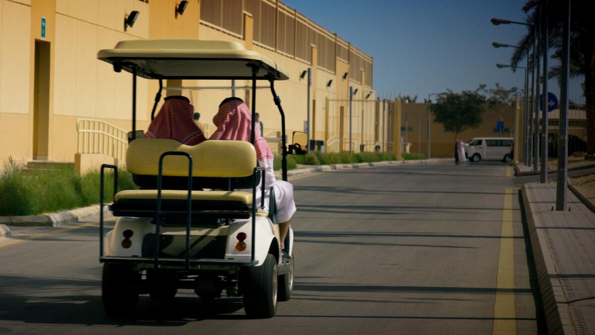 Two figures ride in a gold cart at an imposing compound in Saudi Arabia.