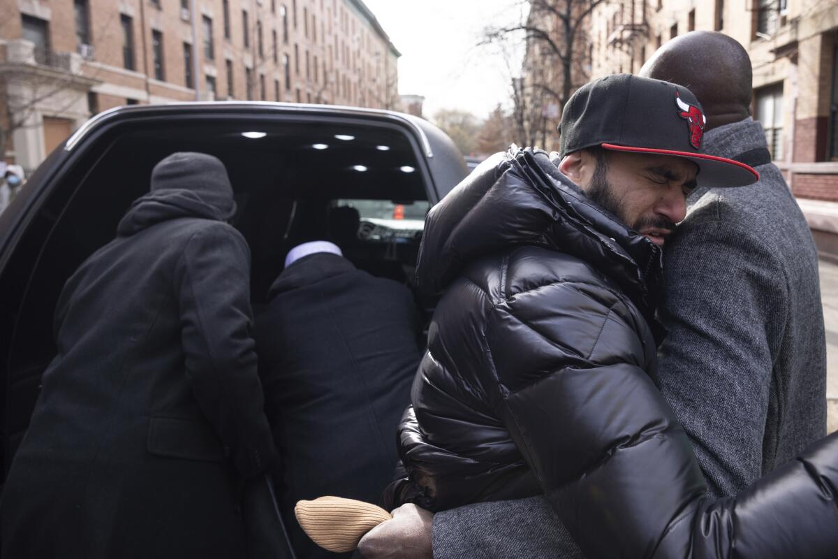 In front of the hearse after the funeral service, a person hugs the father of a 2-year-old who was killed in the fire. 