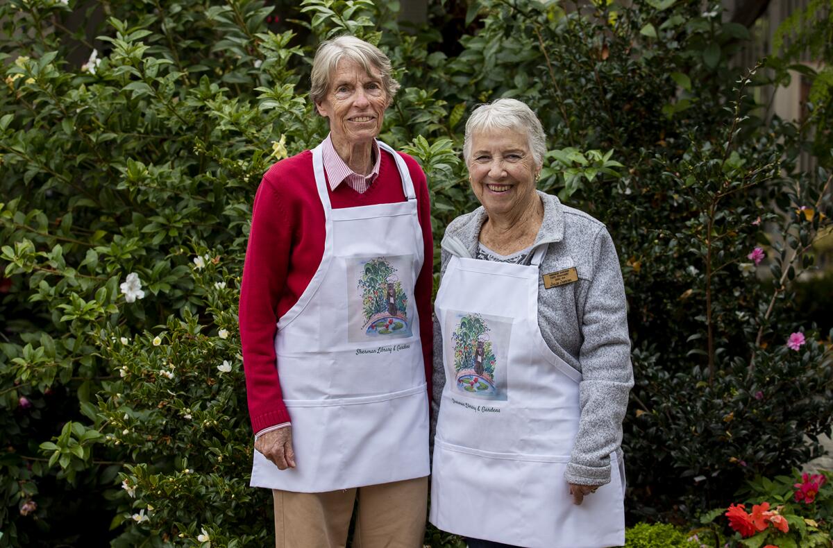 Joan Carter, left, and Julie Jenkins model aprons with the cover art for "First Monday Coffee." 