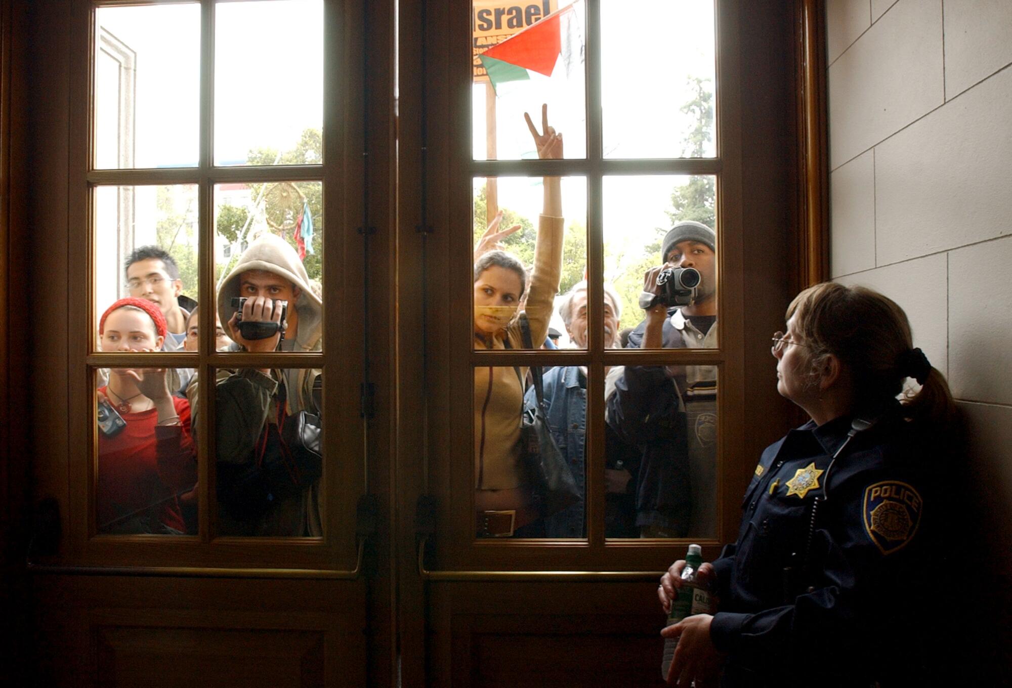 A group of protesters seen through door windows as a policewoman looks out