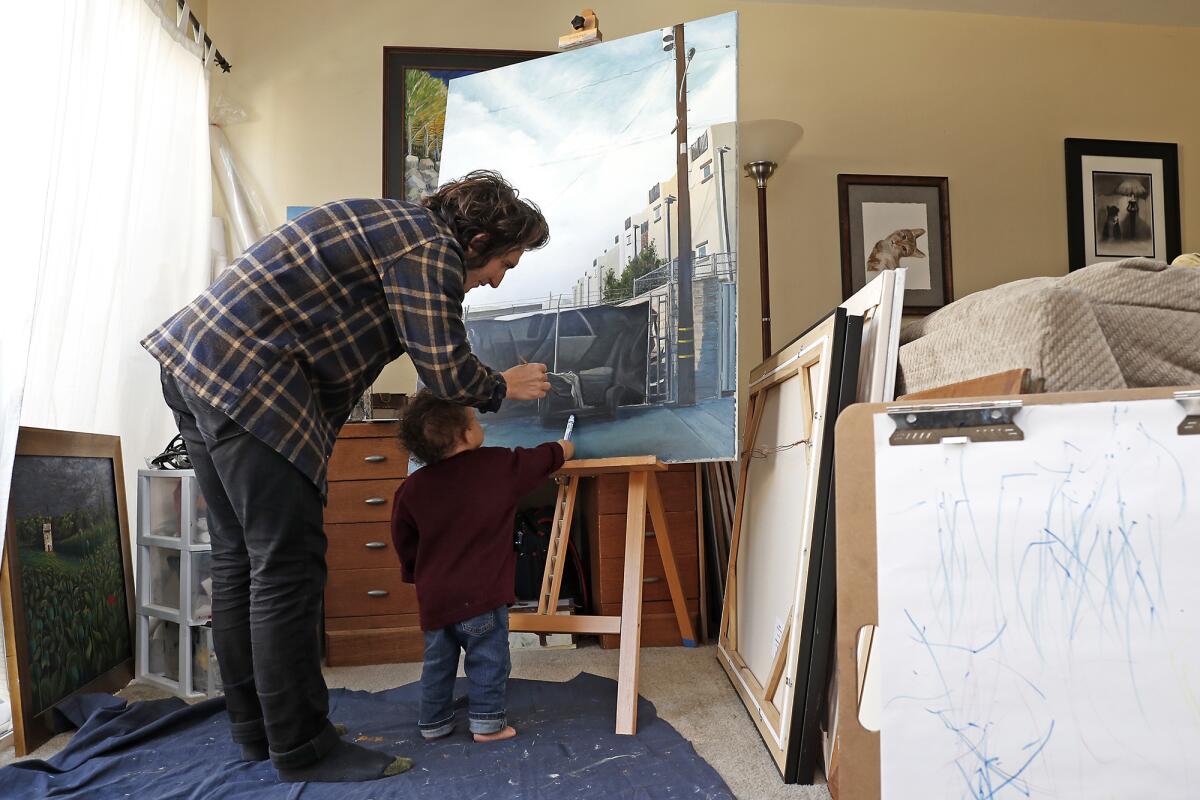 Artist Nico Sauceda spends time with his youngest son, Epic, 18 months, as they create art at their home in Huntington Beach on Thursday. Sauceda's regular job is at a custom framing store, but he's off for at least a month because of the coronavirus outbreak.