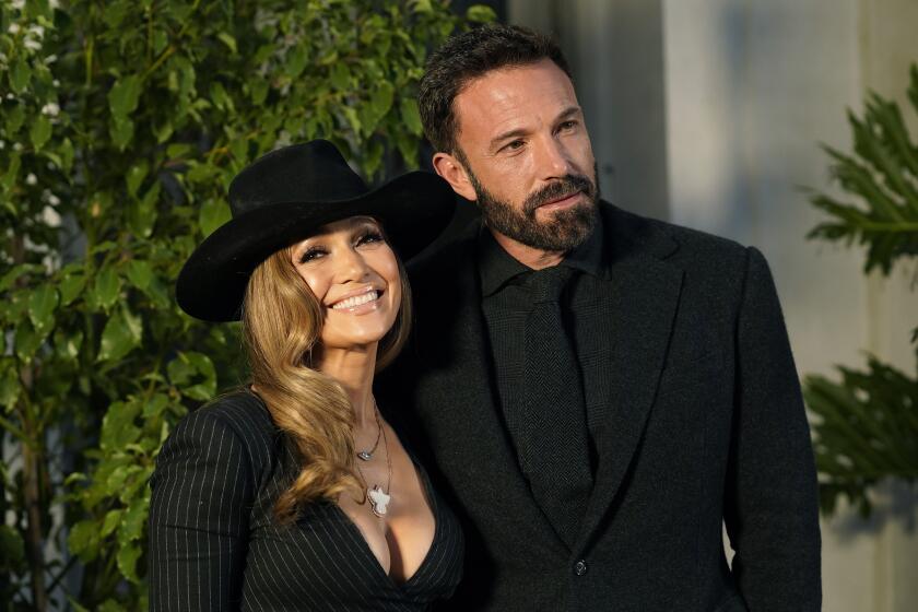 Jennifer Lopez in a black wide-brimmed hat and a black dress with a deep neckline next to Ben Affleck in a black suit