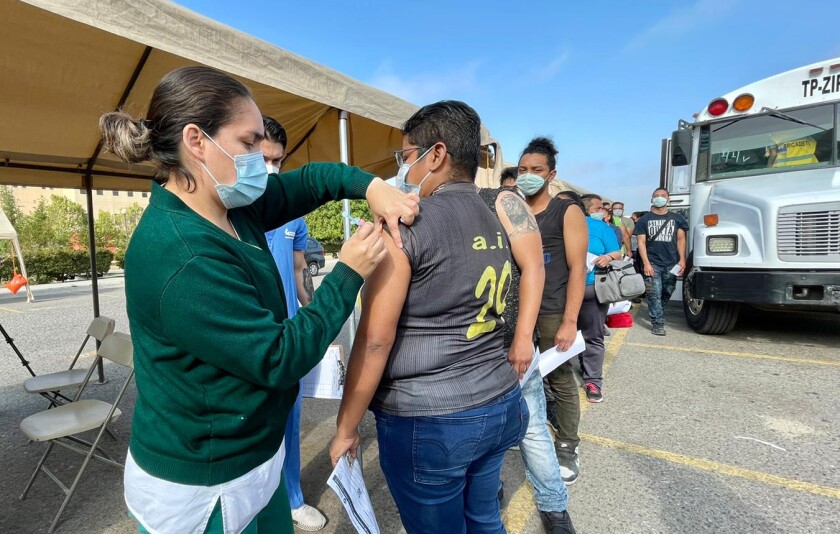 A nurse gives a woman a shot while other people stand in line behind her outside near a bus