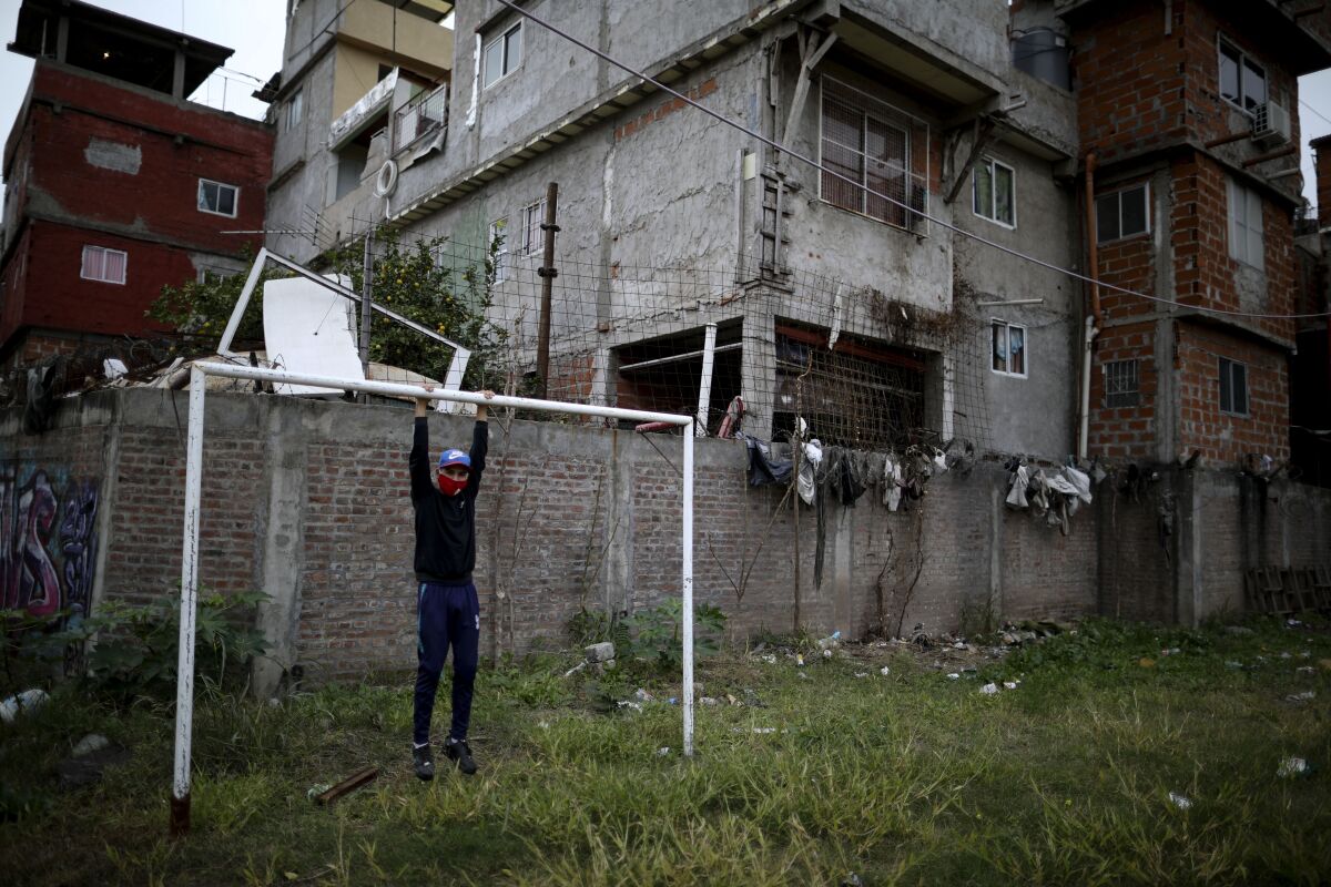 Nicolas Suarez, 16, poses for a photo as he hangs from a soccer goalpost in a soccer field that's closed due to the COVID-19 lockdown in the Fraga neighborhood of Buenos Aires, Argentina, Saturday, June 6, 2020. Suarez, who is recognized as one of the best players in his neighborhood, said that even though he’s afraid of the virus he needs to keep playing, as he has aspirations to go professional. (AP Photo/Natacha Pisarenko)