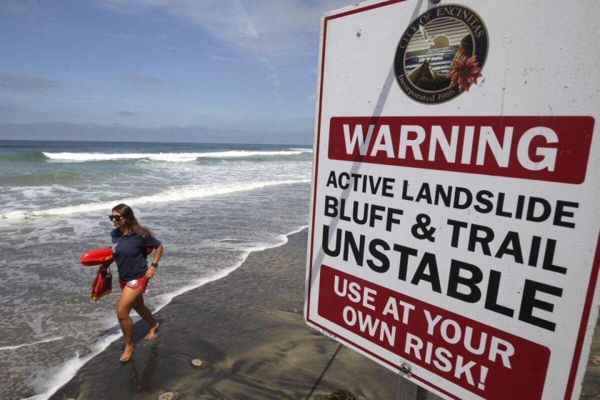 A lifeguard runs past one of several warning signs posted next to the area of the fatal bluff collapse in Encinitas.