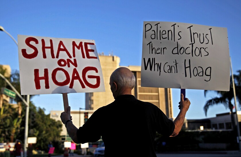 A protester holds one sign that says "Shame on Hoag" and another saying "Patients trust their doctors why can't Hoag."