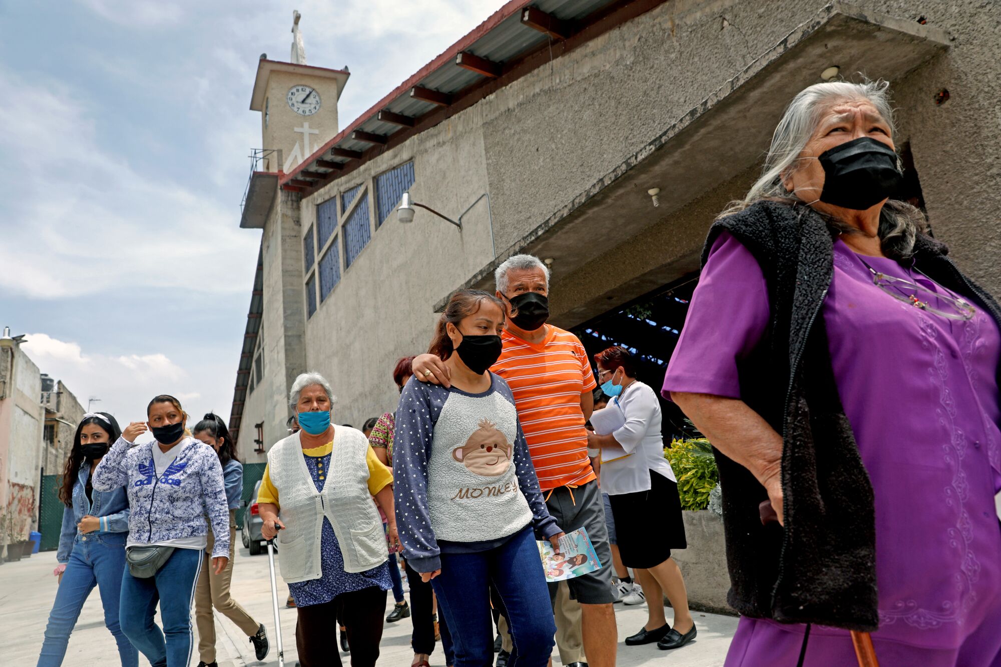 A group of people in masks walk out of a church building