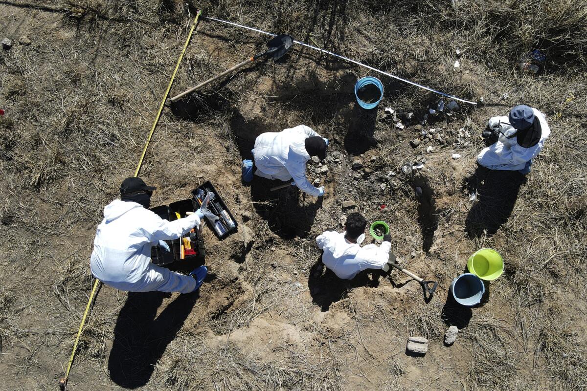 Four people in white coveralls dig in a field on the outskirts of Nuevo Laredo, Mexico.