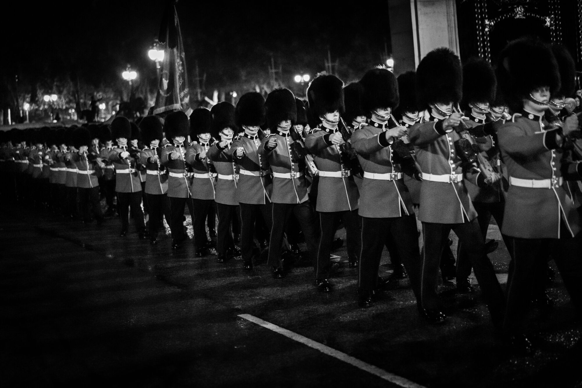 Buckingham Palace guards march in long lines at night.