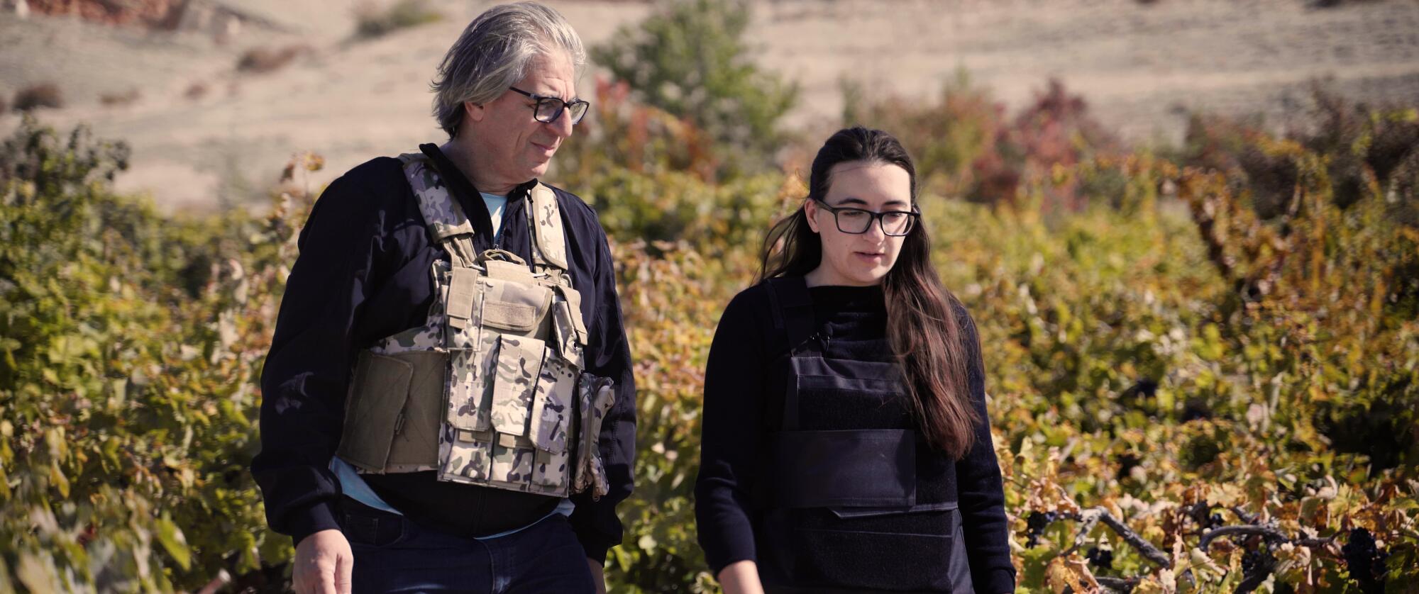 A father and daughter in bulletproof vests walk in their vineyard.