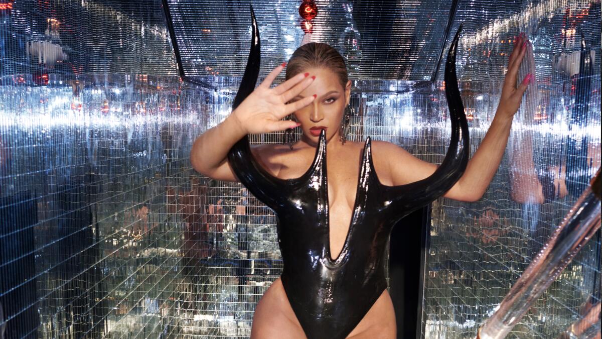 A woman with hair pulled back in a bun wearing a black bodysuit and shielding her eyes from the light in a disco setting